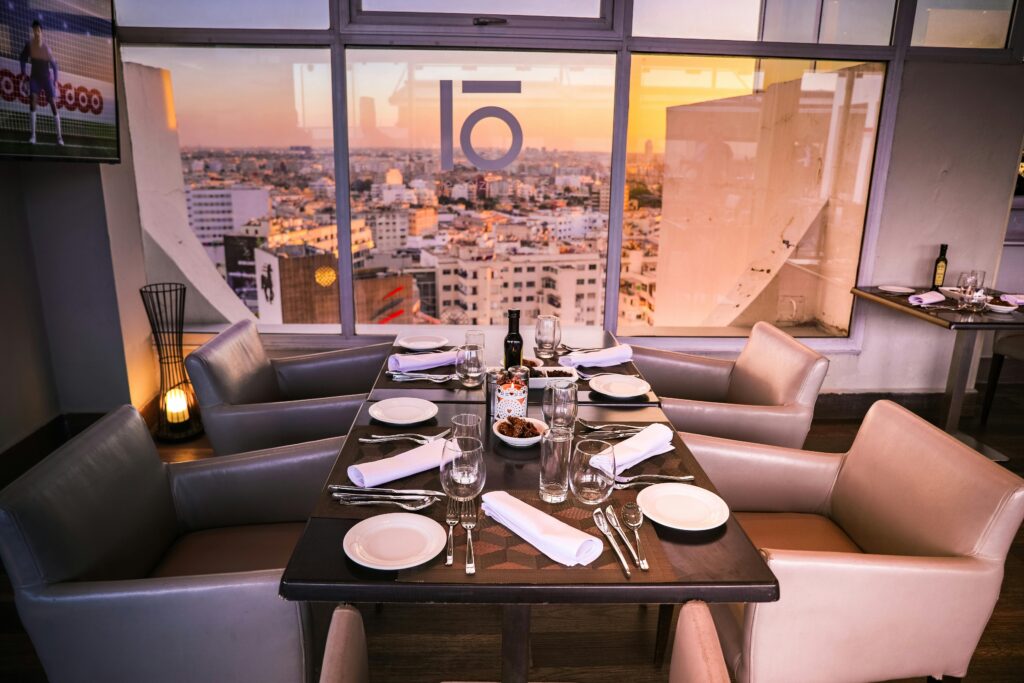 Luxurious dining setup in a modern restaurant overlooking a vibrant cityscape at sunset.